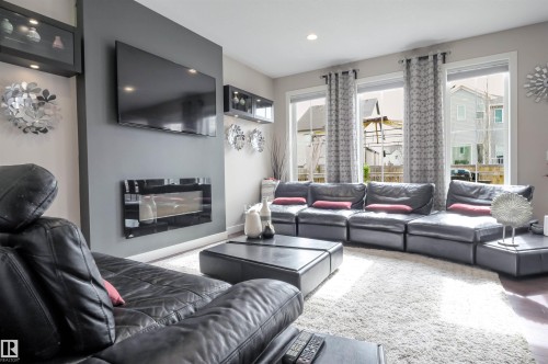 Living area featuring a modern wall-mounted fireplace, recessed lighting, and three large windows providing ample natural light - 1728 53 Street, Edmonton, AB - Indoor Photo Showing Living Room With Fireplace