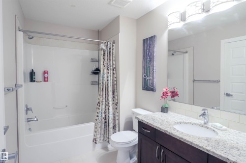 Bathroom featuring a white tub/shower combination with chrome fixtures, a dark wood-finish vanity with a light speckled countertop, an undermount sink, and a large mirror with overhead lighting - 1728 53 Street, Edmonton, AB - Indoor Photo Showing Bathroom
