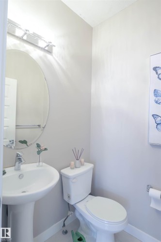 Pedestal sink with chrome faucet, oval mirror, and overhead vanity lighting - 1728 53 Street, Edmonton, AB - Indoor Photo Showing Bathroom