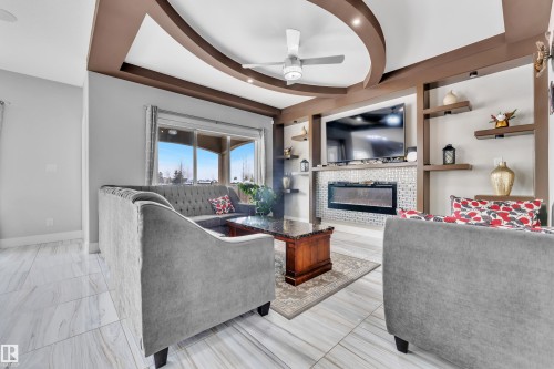 Living area featuring a tray ceiling with recessed lighting, a modern ceiling fan, and large format marble-look tile flooring - 1404 25 Street, Edmonton, AB - Indoor Photo Showing Living Room With Fireplace