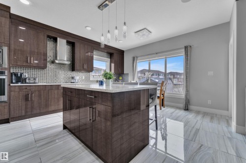 Gleaming kitchen featuring a central island with a light-toned countertop, dark wood-finish cabinetry, and a mosaic tile backsplash - 1404 25 Street, Edmonton, AB - Indoor Photo Showing Kitchen With Upgraded Kitchen