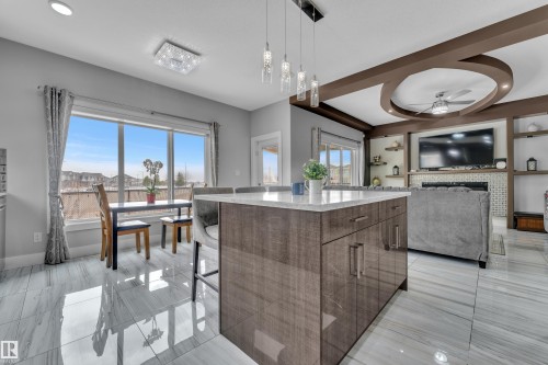 Open-concept living area featuring a kitchen island with stone-finish countertop, polished tile flooring, decorative ceiling details, and a built-in media center with shelving - 1404 25 Street, Edmonton, AB - Indoor