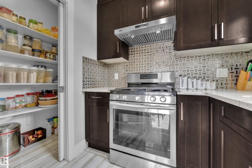 Gourmet kitchen featuring a stainless steel range with matching ventilation hood, dark wood cabinetry, light-toned countertops, and a patterned tile backsplash - 1404 25 Street, Edmonton, AB - Indoor Photo Showing Kitchen