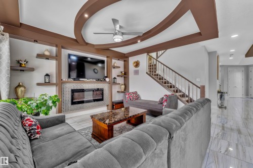 Living area featuring a contemporary ceiling fan, recessed lighting, and a built-in entertainment center with shelving and an electric fireplace set against a mosaic-tiled backdrop - 1404 25 Street, Edmonton, AB - Indoor Photo Showing Living Room With Fireplace