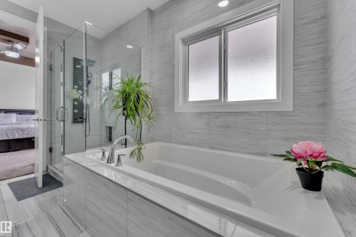 Bathroom featuring a built-in soaking tub with deck-mounted chrome fixtures, a glass-enclosed shower with a multi-function panel, and white-framed privacy windows - 1404 25 Street, Edmonton, AB - Indoor Photo Showing Bathroom