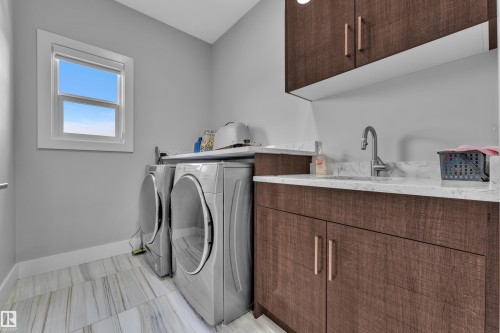 Laundry area featuring a window, wood-finish cabinetry, a built-in sink with a gooseneck faucet, light-toned countertop, and wood-finish flooring - 1404 25 Street, Edmonton, AB - Indoor Photo Showing Laundry Room