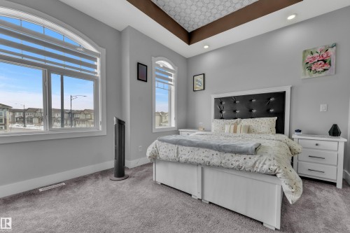 Spacious bedroom featuring arch-top windows with blinds, tray ceiling with recessed lighting, and plush grey carpeting - 1404 25 Street, Edmonton, AB - Indoor Photo Showing Bedroom
