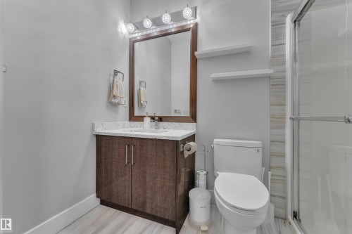 Bathroom featuring a dark wood-finish vanity with a light countertop, a framed mirror, a four-bulb vanity light, a toilet, and a glass-enclosed shower - 1404 25 Street, Edmonton, AB - Indoor Photo Showing Bathroom