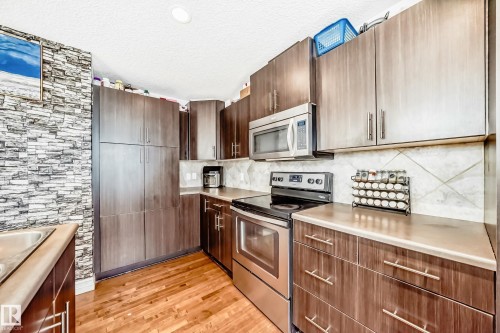 Kitchen featuring wood-finish cabinetry, stainless steel appliances, light-colored countertops, a geometric tile backsplash, and wood-finish flooring - 69 3625 144 Avenue, Edmonton, AB - Indoor Photo Showing Kitchen