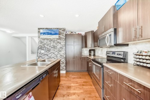 Modern kitchen featuring rich wood-finish cabinetry, stainless steel appliances, and light-toned countertops - 69 3625 144 Avenue, Edmonton, AB - Indoor Photo Showing Kitchen With Double Sink