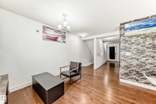 Living area featuring wood-finish flooring, a stacked stone accent wall, and a staircase with a white railing - 69 3625 144 Avenue, Edmonton, AB - Indoor