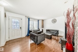 Spacious living area featuring light wood-finish flooring, white walls, and a white paneled entry door with clear glass - 
