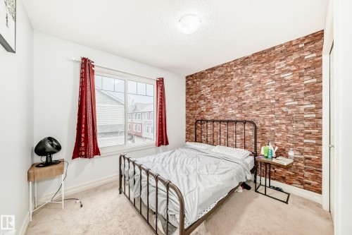 Carpeted room featuring a window with red drapes, a textured accent wall, and a ceiling-mounted light fixture - 69 3625 144 Avenue, Edmonton, AB - Indoor Photo Showing Bedroom