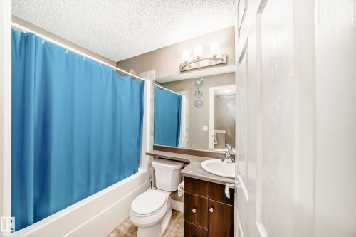 Bathroom featuring a tub/shower combination, vanity with undermount sink, wood-finish cabinetry, and a three-light fixture - 69 3625 144 Avenue, Edmonton, AB - Indoor Photo Showing Bathroom