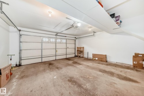 Attached garage featuring a white overhead door with transom-style windows, concrete flooring, and overhead storage shelving - 69 3625 144 Avenue, Edmonton, AB - Indoor Photo Showing Garage
