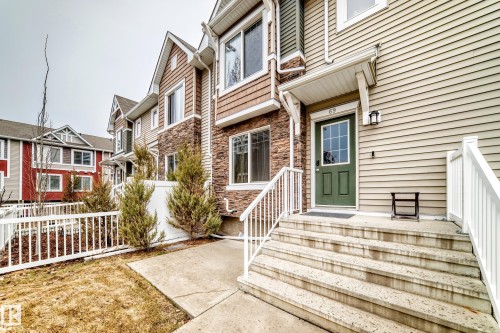 Entryway featuring a dark green door with window panes, concrete steps with white railings, and an outdoor wall sconce - 69 3625 144 Avenue, Edmonton, AB - Outdoor With Facade