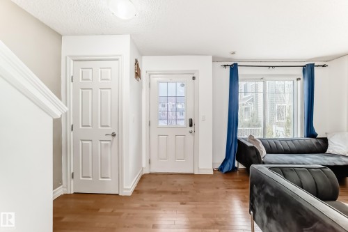 Hardwood-finish flooring throughout, featuring a white paneled door, a glass-paneled entry door, and a large sliding glass door with transom window - 69 3625 144 Avenue, Edmonton, AB - Indoor