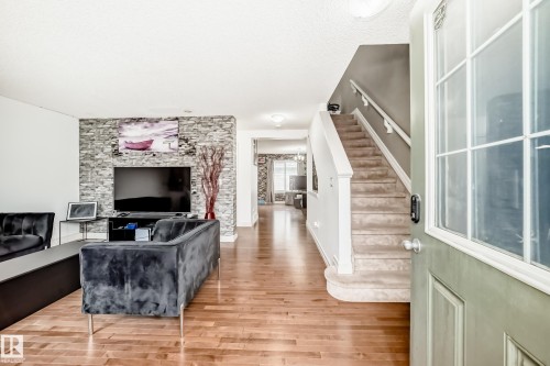 Spacious interior featuring wood-finish flooring, a contemporary stone accent wall, and a carpeted staircase with white railings - 69 3625 144 Avenue, Edmonton, AB - Indoor With Fireplace