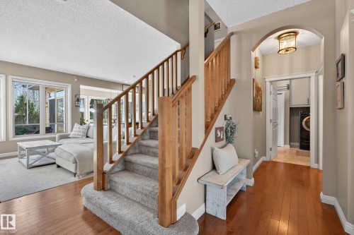 Hardwood flooring entry featuring a carpeted staircase with wood railings, an arched doorway, and recessed laundry area with built-in cabinetry - 1110 Armitage Crescent, Edmonton, AB - Indoor