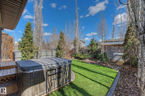 Fenced backyard featuring an artificial turf lawn, a wooden deck, a hot tub with a protective cover, and a wooden storage shed - 1110 Armitage Crescent, Edmonton, AB - Outdoor