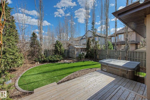 Expansive backyard featuring a large wood-finish deck with built-in hot tub, artificial turf lawn, mature evergreen trees, and a storage shed - 1110 Armitage Crescent, Edmonton, AB - Outdoor With Deck Patio Veranda