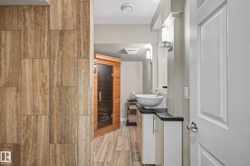Spa-inspired bathroom featuring a built-in sauna with a glass door, a contemporary vessel sink, a dark countertop, and tiled flooring - 1110 Armitage Crescent, Edmonton, AB 