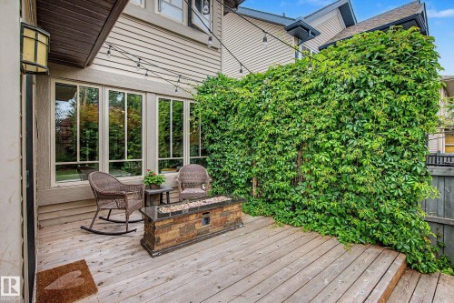 Outdoor deck featuring a wood-plank surface, a stone-finish fire table, and a tall privacy wall covered in abundant greenery - 1110 Armitage Crescent, Edmonton, AB 