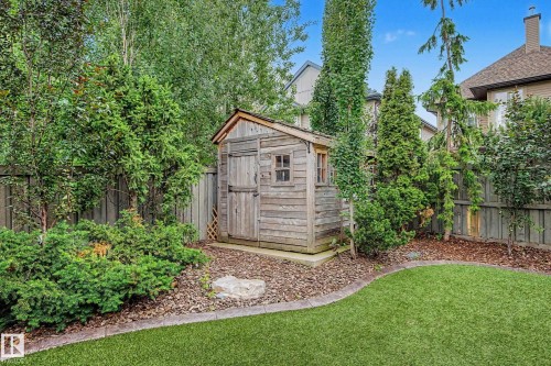Private backyard featuring a wooden shed, mature landscaping, wood chip ground cover, and a manicured lawn with concrete edging - 1110 Armitage Crescent, Edmonton, AB 