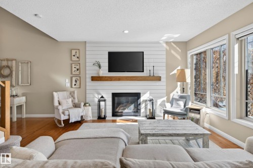 Spacious living area featuring a fireplace with a wood mantle, white shiplap accent wall, hardwood flooring, and multiple large windows - 1110 Armitage Crescent, Edmonton, AB - Indoor Photo Showing Living Room With Fireplace