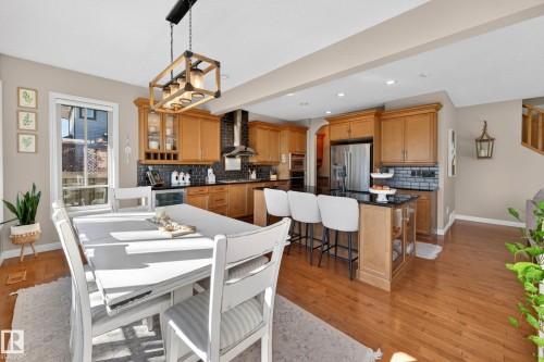 Open-concept kitchen and dining area featuring hardwood flooring, warm wood cabinetry, and a dark tile backsplash - 1110 Armitage Crescent, Edmonton, AB - Indoor Photo Showing Dining Room