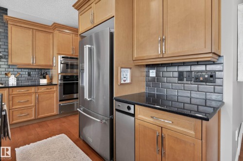 Kitchen featuring wood cabinetry, stainless steel appliances, dark subway tile backsplash, dark countertops, and hardwood flooring - 1110 Armitage Crescent, Edmonton, AB - Indoor Photo Showing Kitchen