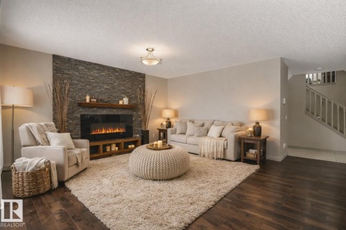 Living room featuring a stacked stone accent wall with an electric fireplace, wood-finish flooring, and a staircase with white railings - 21851 80 Avenue, Edmonton, AB - Indoor Photo Showing Living Room With Fireplace
