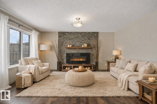 Living space featuring wood-finish flooring, a stone-clad fireplace wall with an electric fireplace, two floating shelves, and an overhead flush-mount light fixture - 21851 80 Avenue, Edmonton, AB - Indoor Photo Showing Living Room With Fireplace