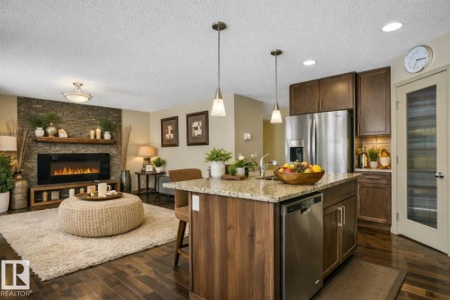 Open-concept living space featuring wood-finish flooring, a stone-accented fireplace wall with integrated shelving, and recessed lighting - 21851 80 Avenue, Edmonton, AB - Indoor Photo Showing Kitchen With Fireplace With Upgraded Kitchen