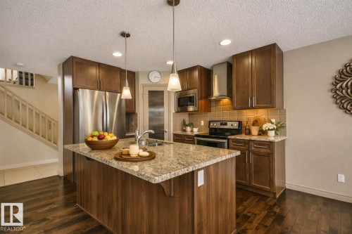 Kitchen featuring a central island with a stone-finish countertop, dark wood-finish cabinetry, stainless steel appliances, a tile backsplash, and recessed lighting - 21851 80 Avenue, Edmonton, AB - Indoor Photo Showing Kitchen With Double Sink With Upgraded Kitchen