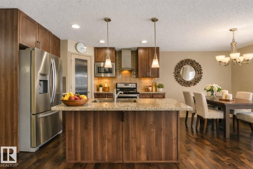 Kitchen featuring a central island with a light-toned countertop, stainless steel appliances, wood-finish cabinetry, and recessed lighting - 21851 80 Avenue, Edmonton, AB - Indoor Photo Showing Kitchen With Upgraded Kitchen