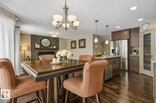 Open concept living area featuring dark wood-finish flooring, a stone-clad fireplace, and a kitchen with dark cabinetry - 21851 80 Avenue, Edmonton, AB - Indoor Photo Showing Dining Room