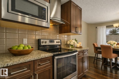 Modern kitchen featuring stainless steel appliances, granite-style countertops, and rich wood-finish cabinetry - 21851 80 Avenue, Edmonton, AB - Indoor Photo Showing Kitchen With Upgraded Kitchen