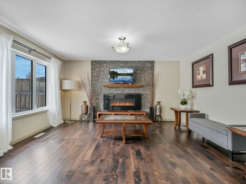 Spacious room featuring wood-finish flooring, a stone-clad fireplace surround with a mounted media display, and a wood mantel - 21851 80 Avenue, Edmonton, AB - Indoor Photo Showing Living Room With Fireplace