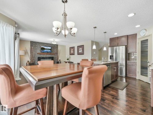 Open-concept living area featuring a stone accent wall with a built-in fireplace and mantel, recessed lighting, wood-finish flooring, a kitchen island with a sink, and stainless steel appliances - 21851 80 Avenue, Edmonton, AB - Indoor Photo Showing Dining Room