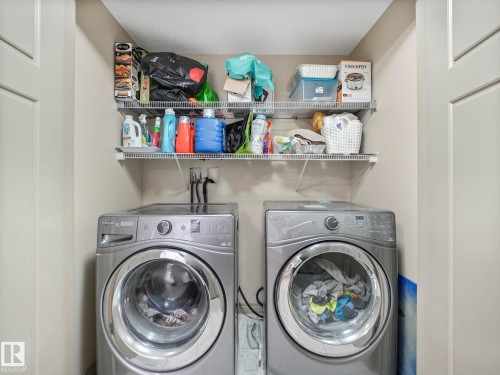 Dedicated laundry area featuring front-loading washer and dryer units, overhead wire shelving for storage, and light-toned wall finishes - 21851 80 Avenue, Edmonton, AB - Indoor Photo Showing Laundry Room