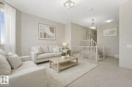 Carpeted living area featuring a large window, neutral wall paint, and a staircase with a light-toned railing - 21851 80 Avenue, Edmonton, AB - Indoor Photo Showing Living Room