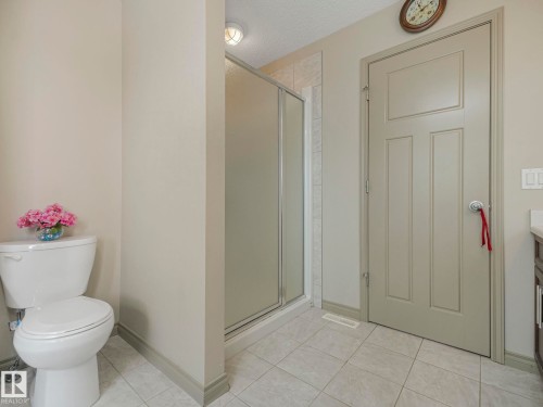 Tiled bathroom featuring a glass-enclosed shower, a white toilet, a panel door, and light-toned walls - 21851 80 Avenue, Edmonton, AB - Indoor Photo Showing Bathroom