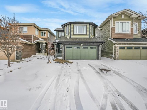 Two-story residence featuring a multi-pane bay window, green garage door, stone accent siding, dark trim, and a shingle roof - 21851 80 Avenue, Edmonton, AB - Outdoor With Facade