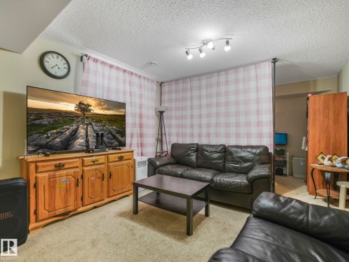 Carpeted room featuring a ceiling-mounted track light fixture, plaid curtains on a ceiling-mounted rod, and a wood-finish media console - 21851 80 Avenue, Edmonton, AB - Indoor Photo Showing Living Room