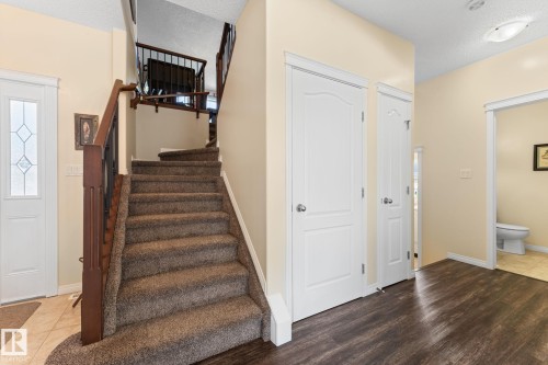 Inviting entryway featuring a carpeted staircase with dark wood railings, a white paneled door with decorative glass, and contrasting dark wood flooring - 112 Lakeland Point(E), Beaumont, AB - Indoor Photo Showing Other Room