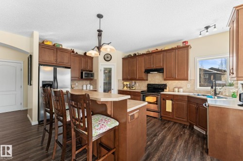 Well-appointed kitchen featuring dark wood cabinetry, stainless steel appliances, a center island with seating, and dark wood-style flooring - 112 Lakeland Point(E), Beaumont, AB - Indoor Photo Showing Kitchen With Double Sink