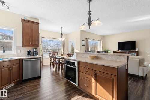 The spacious kitchen features wood cabinetry, a stainless steel dishwasher, and a center island with an integrated oven and counter seating - 112 Lakeland Point(E), Beaumont, AB - Indoor Photo Showing Kitchen