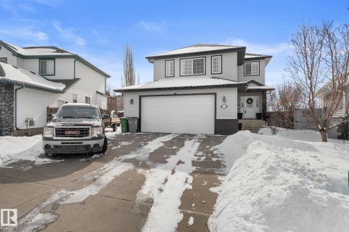 The property features a two-story exterior with light gray siding and dark trim, a white garage door, and a covered front entrance - 112 Lakeland Point(E), Beaumont, AB - Outdoor With Facade