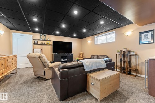 Living area featuring a black grid ceiling with recessed lighting, beige walls, and carpet flooring - 112 Lakeland Point(E), Beaumont, AB - Indoor Photo Showing Basement